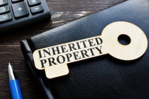 Wooden key-shaped tag with the words "inherited property" on a black leather-bound book, adjacent to a calculator and a pen, symbolizing financial planning or settlement of an estate.