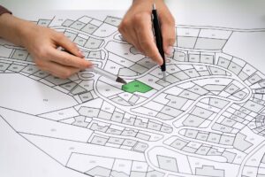 Person reviewing a detailed land development map with plotted lots, using a pencil and a ruler for precision to provide legal services.