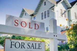 Signs of a successful sale: a 'sold' sticker prominently displayed over a 'for sale' sign in front of a picturesque two-story house on a sunny day, showcasing the successful legal representation through
